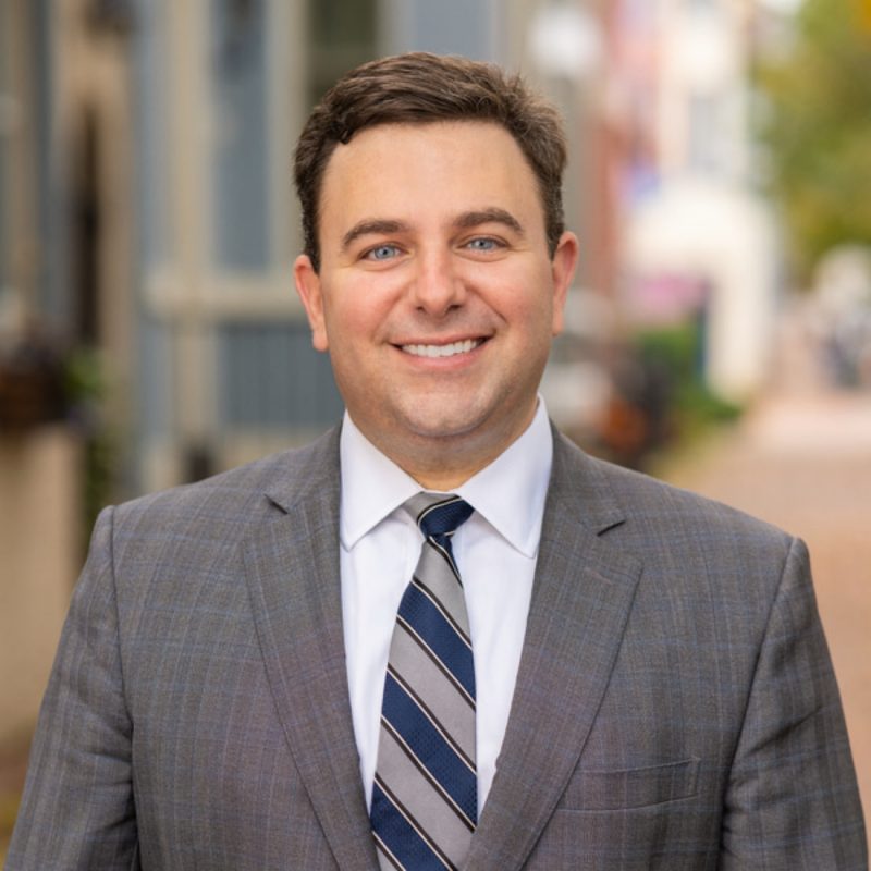 Portrait of Chris Itteilag, Washington DC luxury real estate agent, in a grey suit and striped navy tie